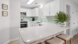 Una cocina moderna con armarios blancos, una isla central con taburetes y una planta en maceta.