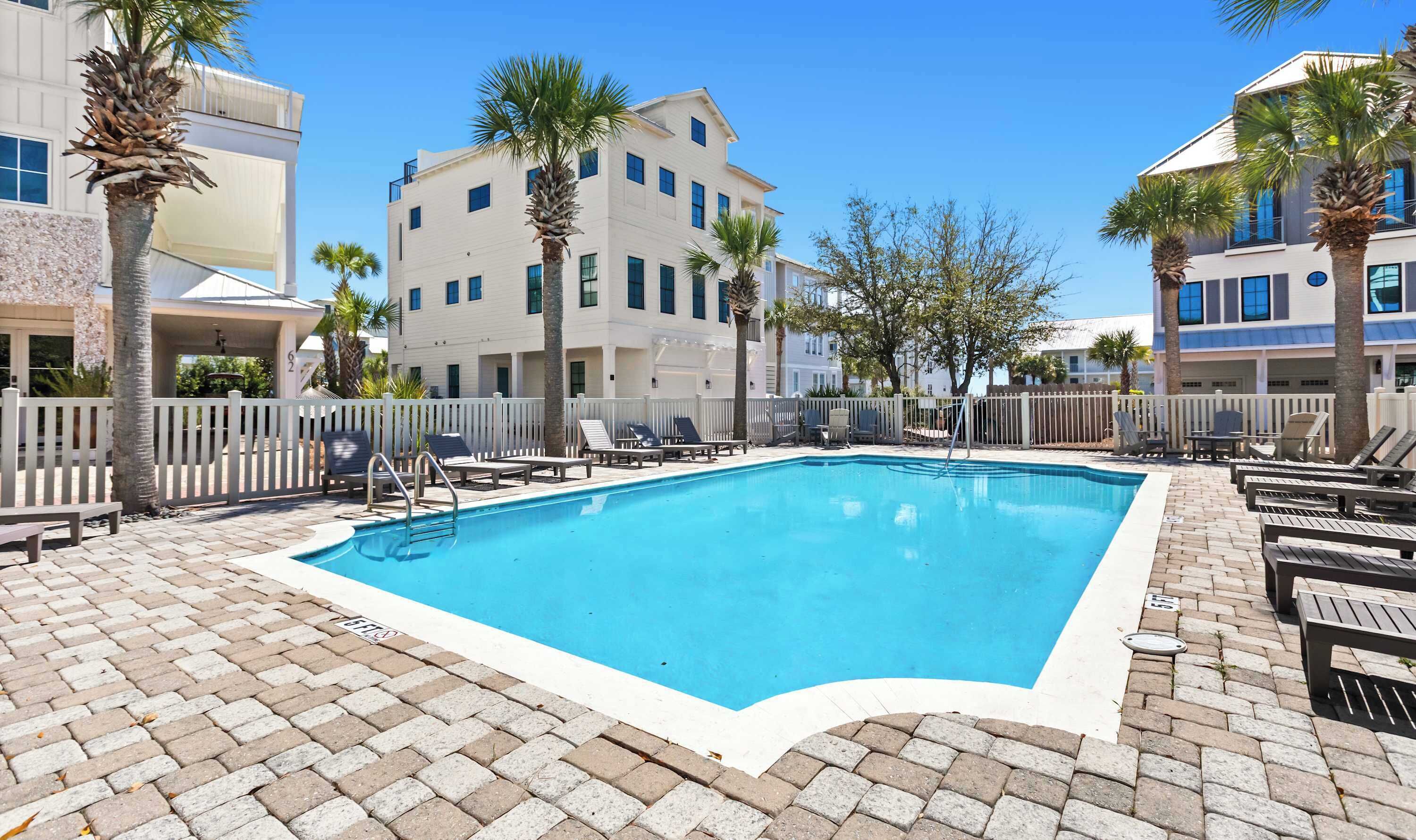 A rectangular swimming pool with a white border, surrounded by lounge chairs and palm trees.