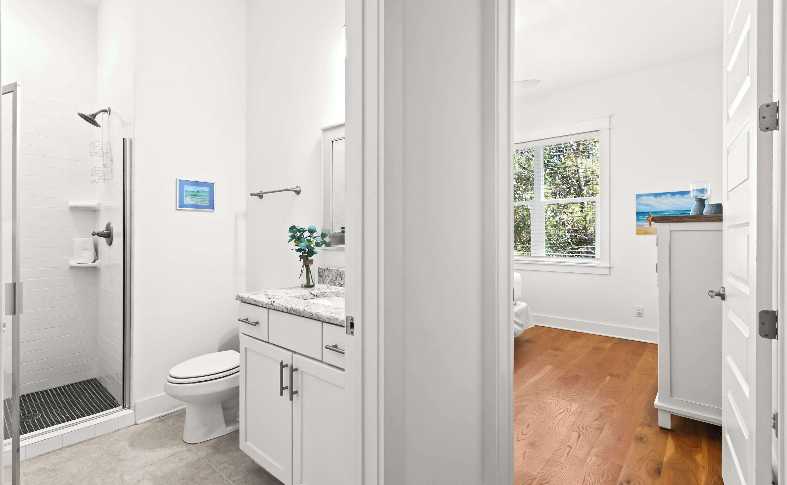 Une salle de bain avec douche, toilettes et lavabo, un plancher en bois et une fenêtre avec stores.