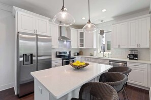 A modern kitchen with white cabinets, stainless steel appliances, a central island with wicker chairs, and pendant lighting. - Inlet Beach Home with Shared Pool, Cart & Bikes (Inlet Beach)