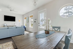 Ein modernes Wohnzimmer mit einem Holzesstisch, einem blauen Sofa und einem an der Wand befestigten Fernseher.