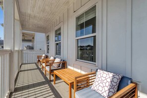 Eine überdachte Veranda mit Holzmöbeln, darunter Bänke und ein Tisch, sowie große Fenster.