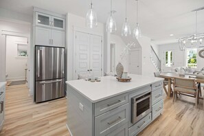 Eine moderne Küche mit einem Edelstahl-Kühlschrank, grauen Schränken und einer zentralen Kochinsel mit weißer Arbeitsplatte.