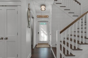 Ein Flur mit einer Treppe, einem Schild mit der Aufschrift 'Beach House' und einer Tür mit einem Fenster.