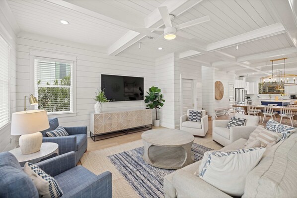 A spacious living room with a large TV, comfortable seating, a dining area, and a kitchen. - Destin Home for Groups with Pool & Game Room (Destin)