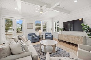 A spacious living room with a large TV, comfortable seating, and a ceiling fan. - Destin Home for Groups with Pool & Game Room (Destin)