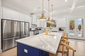A modern kitchen with stainless steel appliances, a marble island, and pendant lighting. - Destin Home for Groups with Pool & Game Room (Destin)