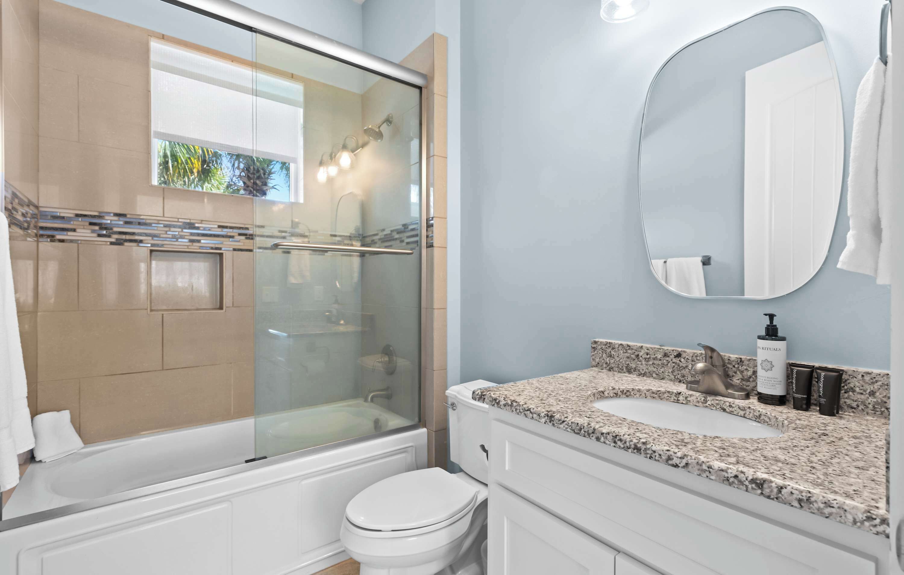 A bathroom with a glass-enclosed shower, a white toilet, a granite countertop sink, a large mirror, and a towel rack.
