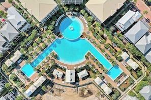 Ein Luftbild eines Resorts mit einem zentralen Schwimmbad, mehreren Liegebereichen und umliegenden Palmen.