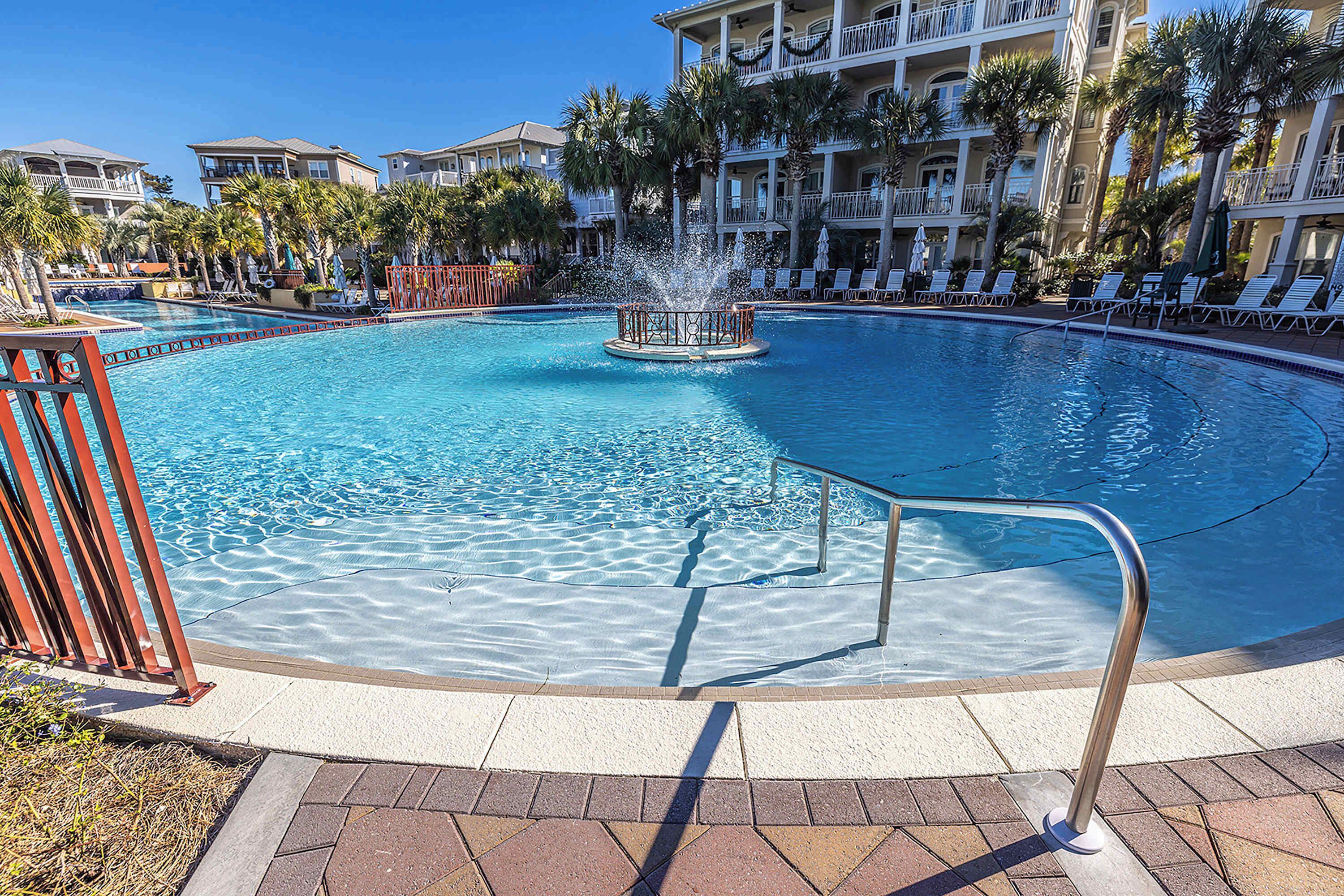 A large pool with a central fountain, surrounded by lounge chairs and palm trees.