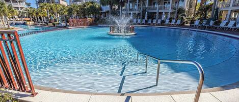 A large pool with a central fountain, surrounded by lounge chairs and palm trees.