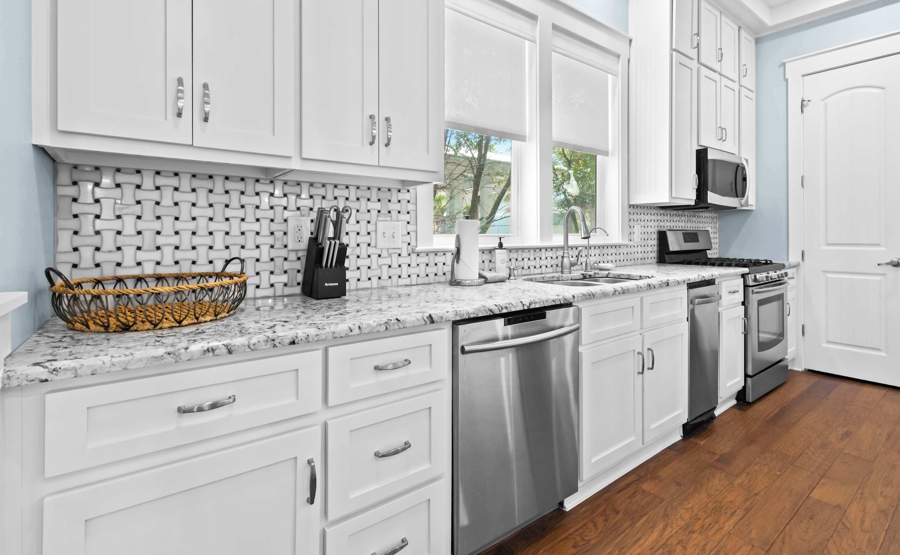 A kitchen with white cabinets, a granite countertop, stainless steel appliances, and a window with a view of trees.