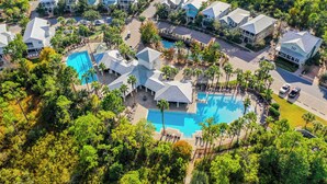 Luftaufnahme eines Resorts mit mehreren Gebäuden, einem zentral gelegenen Schwimmbecken und umliegender Bepflanzung.