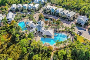 Luftaufnahme eines Resorts mit mehreren Gebäuden, einem zentral gelegenen Schwimmbecken und umliegender Bepflanzung.