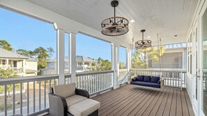 Eine überdachte Veranda mit Korbmöbeln, einem blauen Sofa und Blick auf angrenzende Häuser.