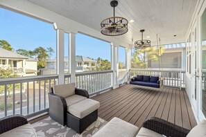 Eine überdachte Veranda mit Korbmöbeln, einem blauen Sofa und Blick auf angrenzende Häuser.