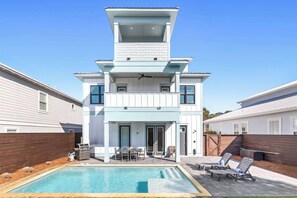 Ein modernes, zweistöckiges Haus mit Swimmingpool, Sitzgelegenheiten im Freien und einer Grillanlage.