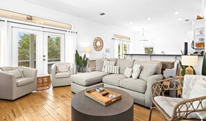 A modern living room with a sectional sofa, a round coffee table, and a dining area with a kitchen in the background. - Santa Rosa Home with Pool, Deck & Beach Access (Santa Rosa Beach)