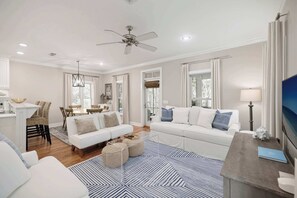 Ein geräumiges Wohnzimmer mit einem weißen Sofa, einem Essbereich mit Tisch und Stühlen sowie einem Deckenventilator.