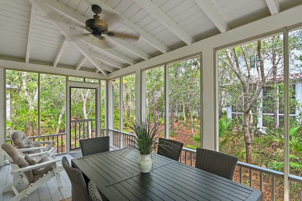 Ein überdachter Außenbereich mit Tisch und Stühlen, großen Fenstern und einem Deckenventilator.