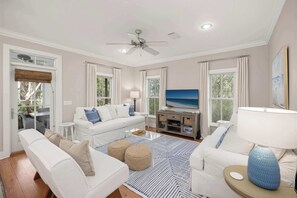 Ein Wohnzimmer mit einem weißen Sofa, einem Couchtisch, einem Fernseher und einem Deckenventilator.