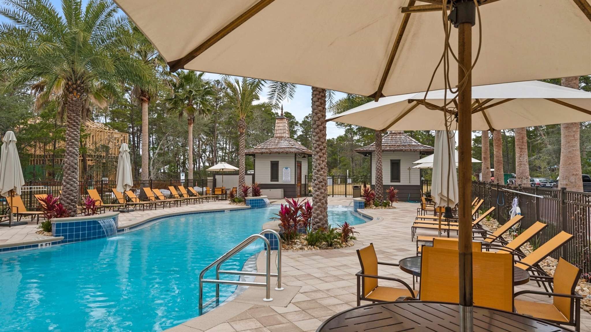 A pool area with lounge chairs, umbrellas, and a small building.