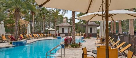 A pool area with lounge chairs, umbrellas, and a small building.