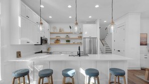 A modern kitchen with white cabinetry, a central island with bar stools, stainless steel appliances, and pendant lighting. - Vitamin Sea Home with Golf Cart & Shared Pool (Watersound)