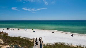 A beach with a wooden pier leading to a sandy shore, clear blue water, and a few beach umbrellas. - Vitamin Sea Home with Golf Cart & Shared Pool (Watersound)