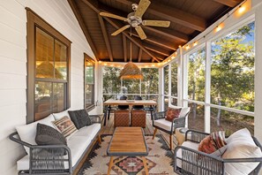 Eine überdachte Veranda mit Deckenventilator, einem Esstisch mit Stühlen und einer Couch mit Kissen.