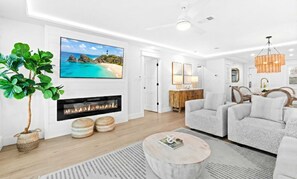 Ein modernes Wohnzimmer mit Kamin, Wand-Fernseher und Essbereich mit Stühlen und Tisch.