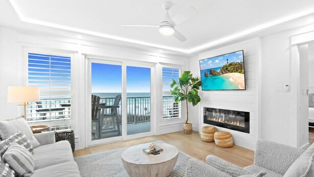 Ein modernes Wohnzimmer mit Kamin, großem Fernseher und einem Balkon mit Meerblick.