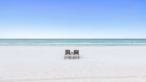 Ein Strand mit zwei Holzstühlen, die zum Meer blicken.