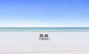 Ein Strand mit zwei Holzstühlen, die zum Meer blicken.