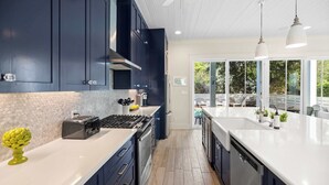 Une cuisine moderne avec des meubles bleu foncé, un plan de travail blanc et une vue sur l’extérieur.