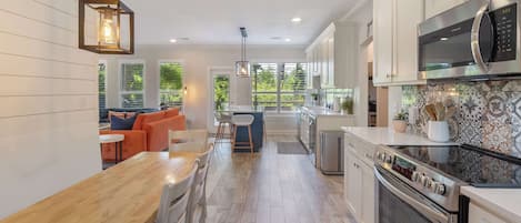 Una cocina moderna con armarios blancos, un microondas de acero inoxidable y un horno. Hay una mesa de comedor de madera con sillas y una isla de cocina con taburetes.