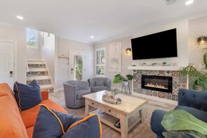 Ein Wohnzimmer mit Kamin, einem an der Wand montierten Fernseher und einer Treppe, die eine weitere Ebene hinaufführt.