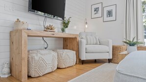 Un soggiorno moderno con un tavolo consolle in legno, una poltrona bianca, una TV a schermo piatto montata a parete e un piccolo tavolino con oggetti decorativi.