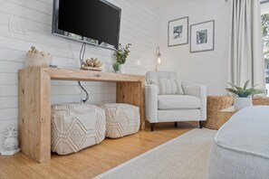 Ein modernes Wohnzimmer mit einem Holzkonsolentisch, einem weißen Sessel, einem flachbildfernseher an der Wand und einem kleinen Beistelltisch mit Dekorationen.