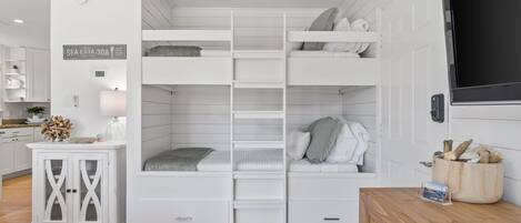 Una cama con literas y cajones para guardar cosas, un armario de madera, un televisor y un cartel en la pared.