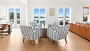 A spacious living room with a view of a lake, a dining area with a table and chairs, and a kitchen area. - Oyster Lake Estate with Pool, Dock & Golf Cart (Santa Rosa Beach)
