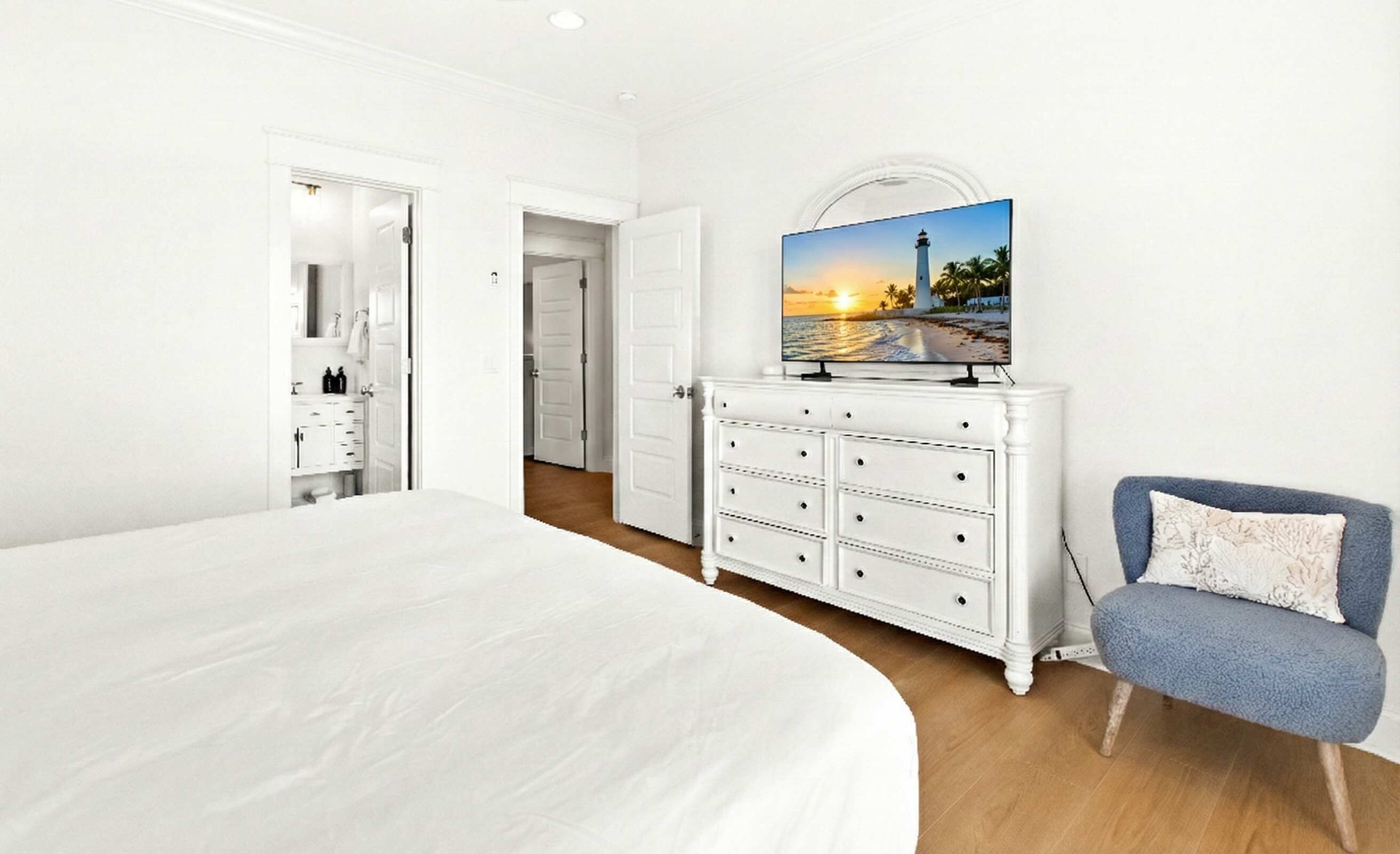 A bedroom with a large bed, a dresser, a television on a stand, and a chair.