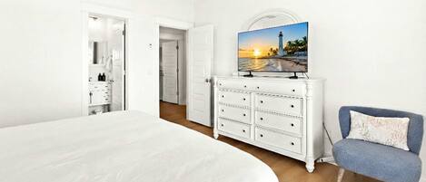 A bedroom with a large bed, a dresser, a television on a stand, and a chair.