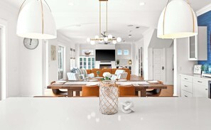A spacious dining area with a wooden table, white chairs, and pendant lighting. - Oyster Lake Estate with Pool, Dock & Golf Cart (Santa Rosa Beach)