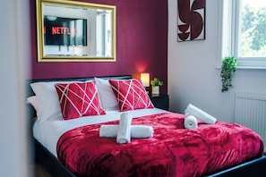Ein ordentlich bezogenes Bett mit roter und weißer Bettwäsche, ein Spiegel mit einer Neonreklame und ein großes abstraktes Gemälde an der Wand.