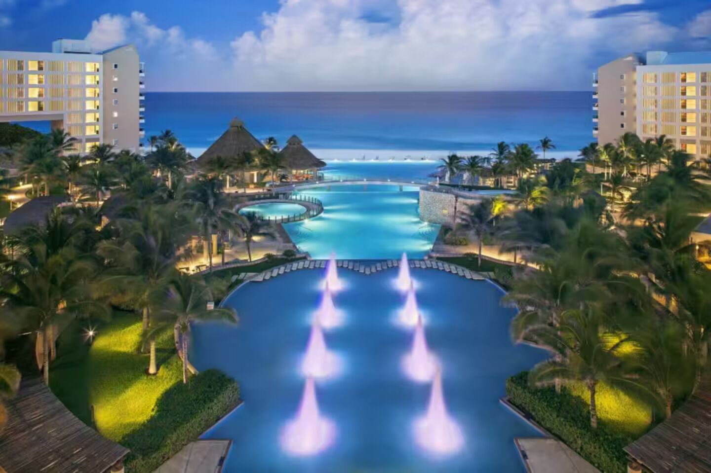 Un complex turístic amb una piscina central, palmeres i vistes a l'oceà.