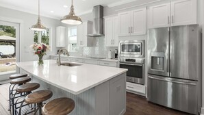 A modern kitchen with white cabinetry, stainless steel appliances, and a large island with stools. - Sea Change Home with Pool, Lake Access & Golf Cart (Santa Rosa Beach)