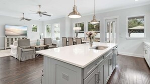 A spacious kitchen with a large island, pendant lighting, ceiling fans, and a dining area with chairs and a table. - Sea Change Home with Pool, Lake Access & Golf Cart (Santa Rosa Beach)