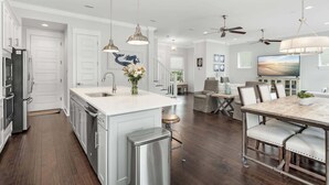 A modern kitchen with stainless steel appliances, a central island, pendant lighting, and a dining area with a marble table and chairs. - Sea Change Home with Pool, Lake Access & Golf Cart (Santa Rosa Beach)