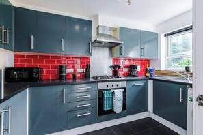 A modern kitchen with teal cabinets, a red backsplash, and a gas stove.